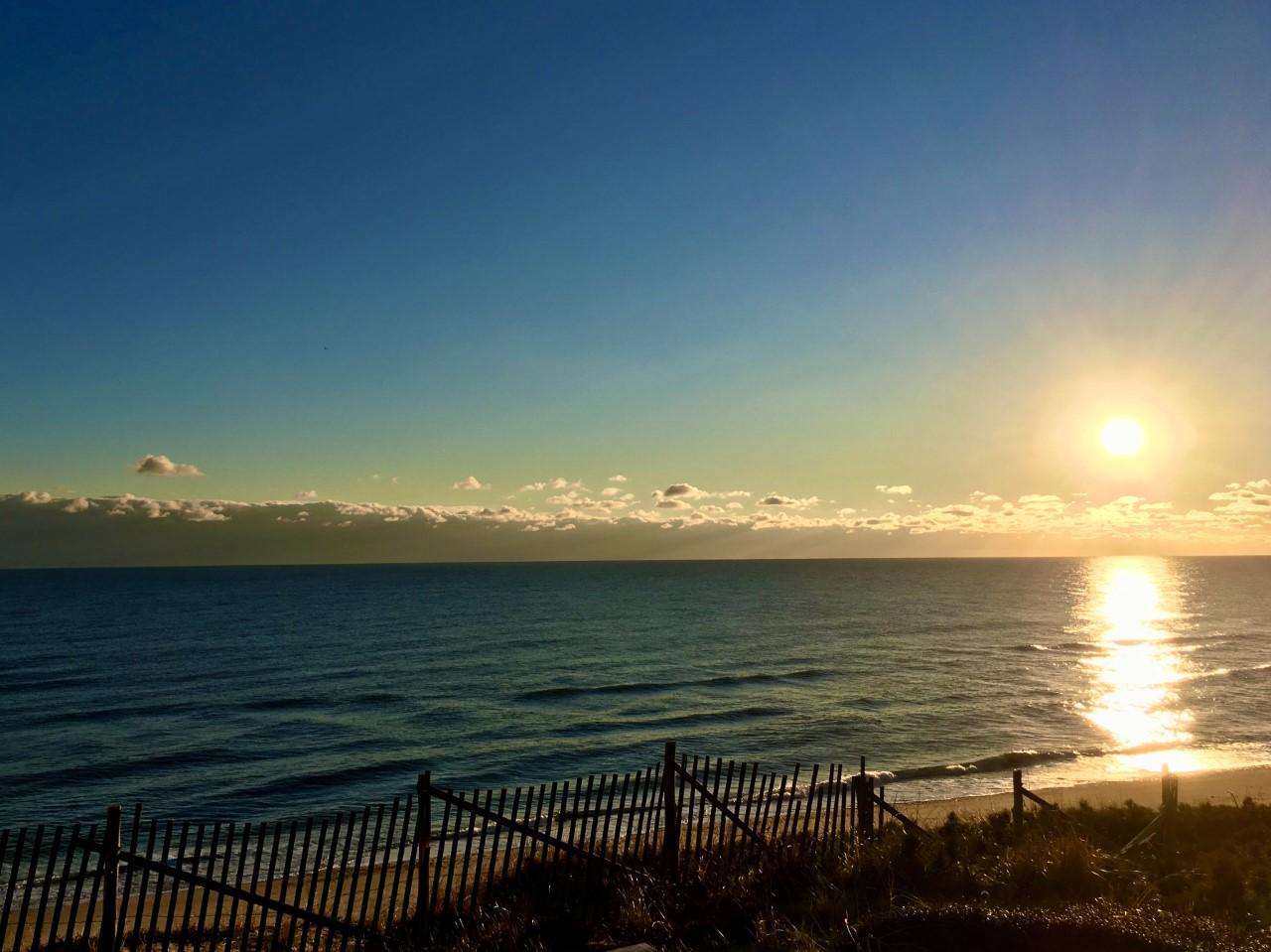 A brilliant sun rises over the ocean reflecting light on the water's surface.