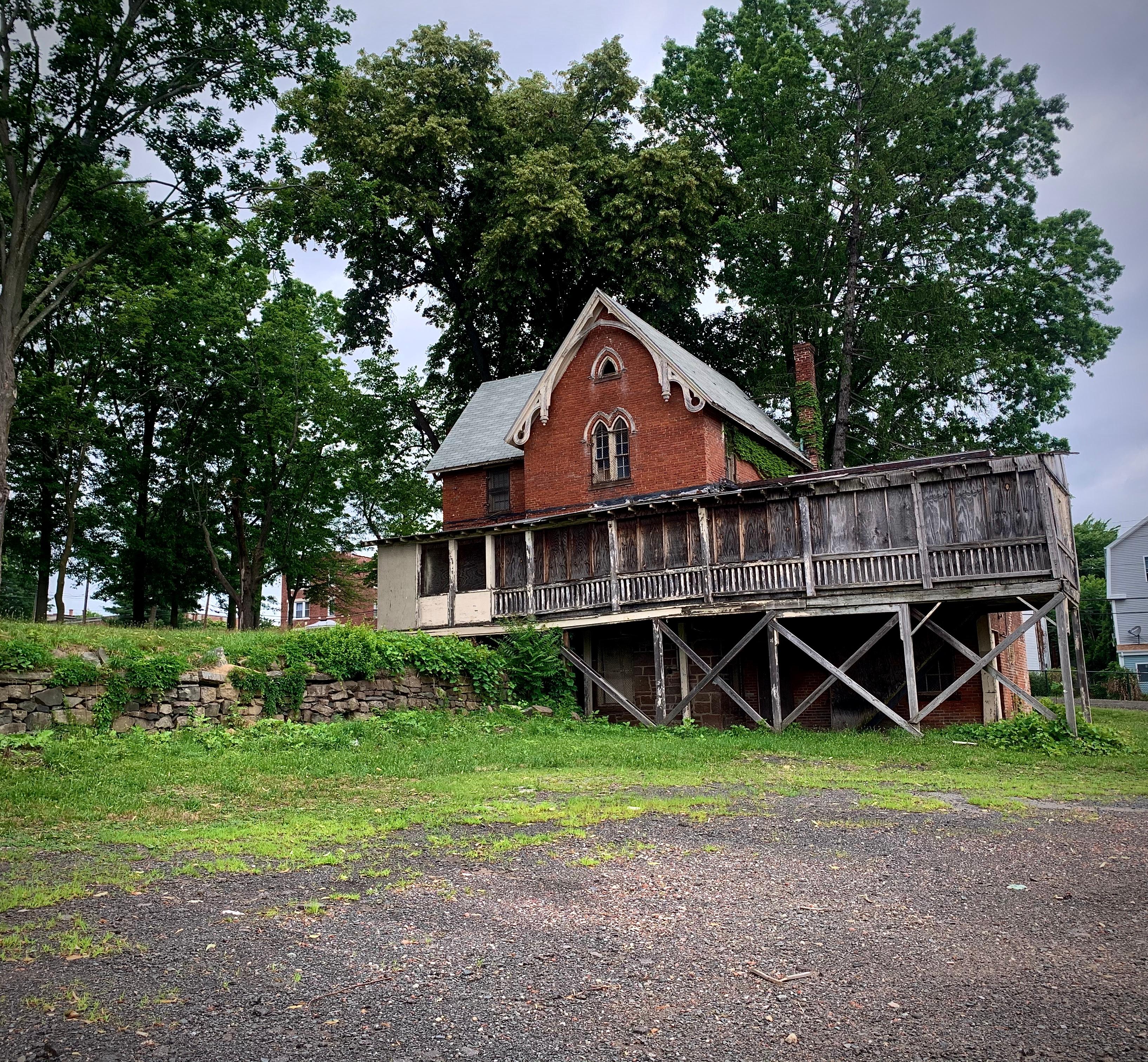 A red brown building with a wooden enclosed spaced in front of trees on a cloudy day.