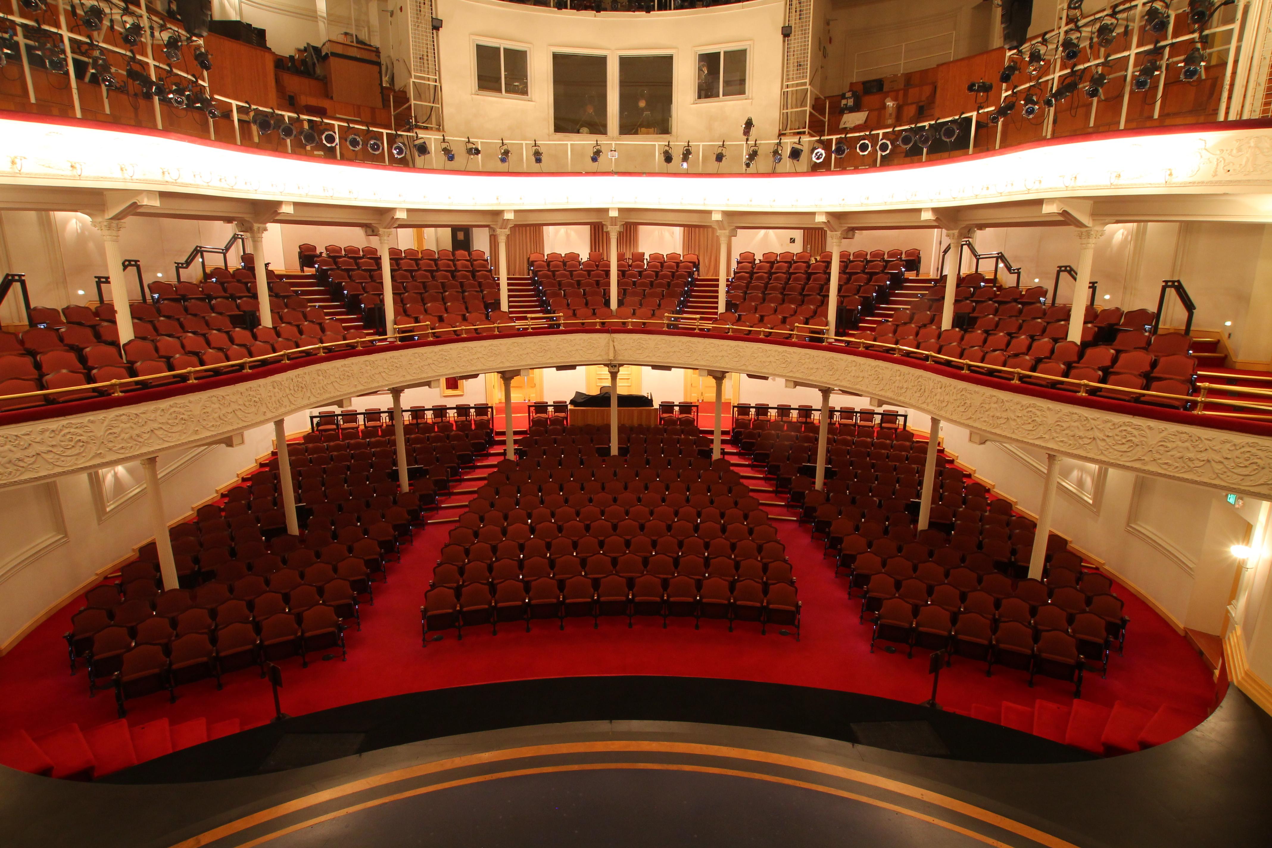 Three levels of auditorium style seating with red carpeting and upholstered seats