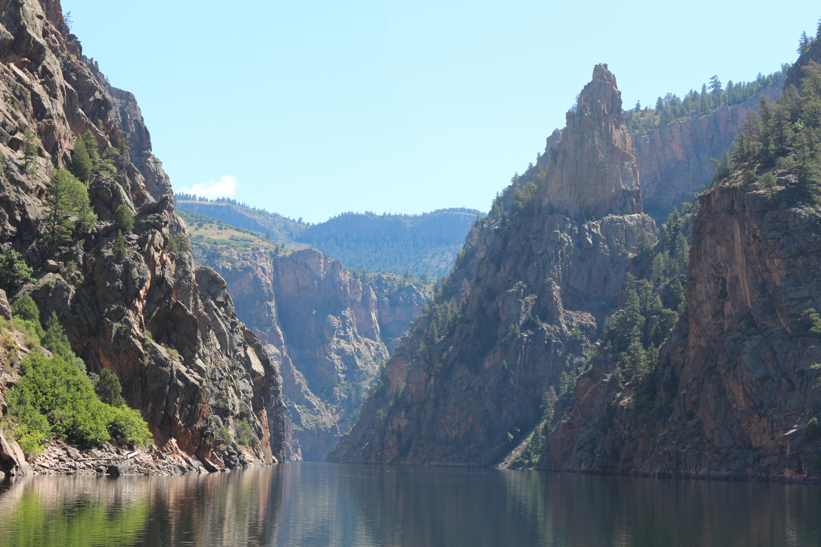 Tall spires alongside steep canyon walls. A narrow body of water flows below.