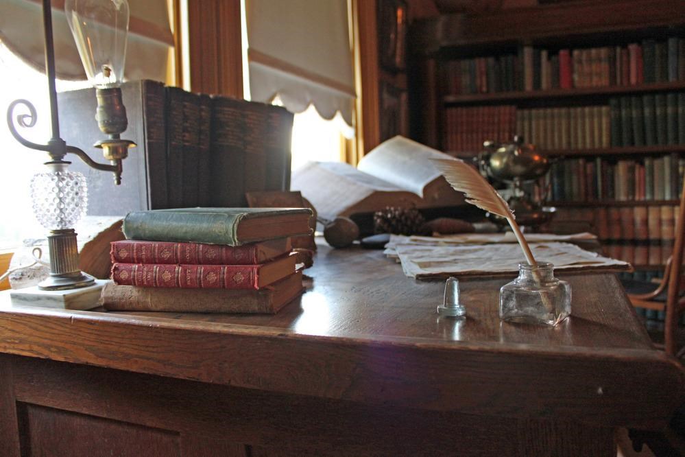 Old books, a writing pen and inkwell, and paper sit on John Muir's original desk. 