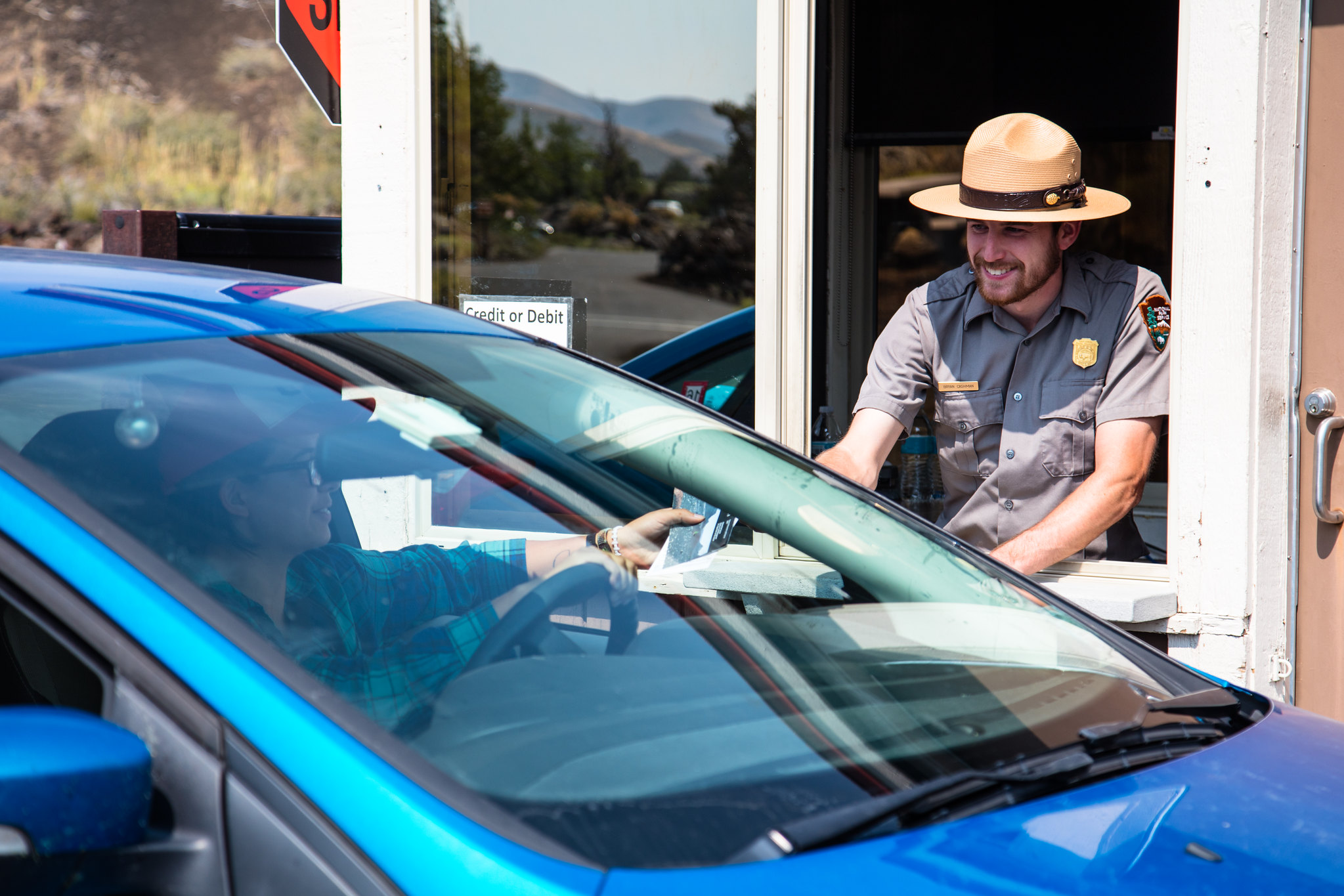 Ranger leans out of an entance station window and hands a pamphlet to a guest in a vehicle.