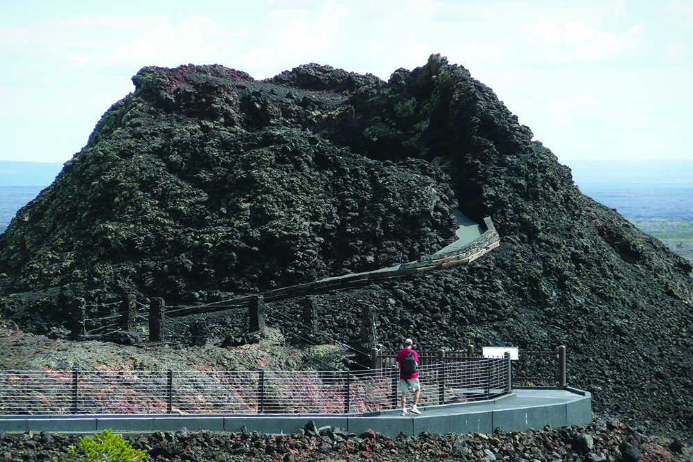 Hiker on the accessible trail to the Snow Cone with the Spatter Cones behind.