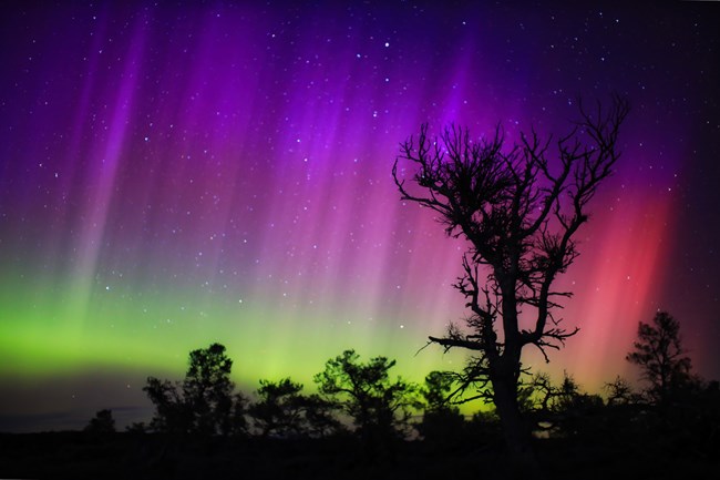 Northern Lights over a silhouetted landscape.