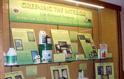 Containers of green cleaning products in a display case with signs explaining them.