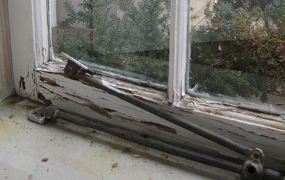 Close-up of the interior of a window painted white and with peeling paint and broken window-opening hardware.