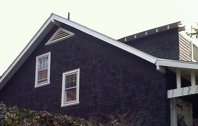 Gable end of a grey house with two windows and a triangular louvered vent at the peak of the roof.