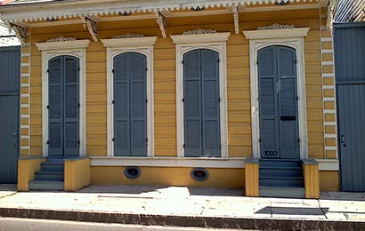 Yellow frame house with shutters closed across the windows and oval openings in the foundation to provide ventilation.
