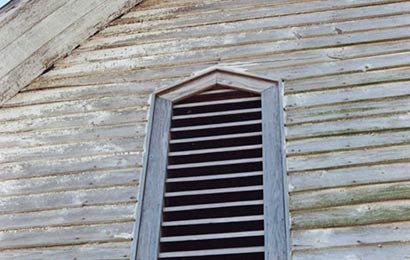 Louvered vent in the end of a frame barn.