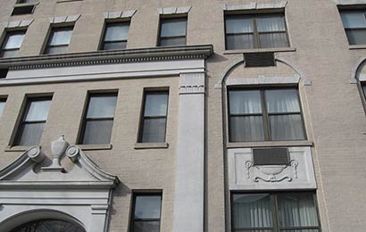 Rectangular openings cut through decorative arches and panels of a masonry building to install air conditioning units.