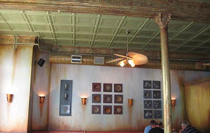 Mechanical ductwork painted to match the adjacent historic metal ceiling panels and friezes.