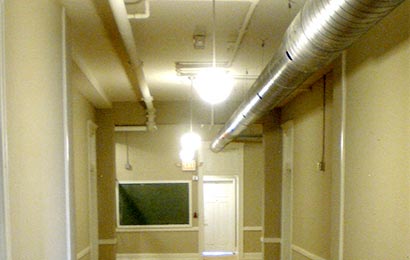 Large, unpainted ductwork installed in the corridor of a rehabilitated building.