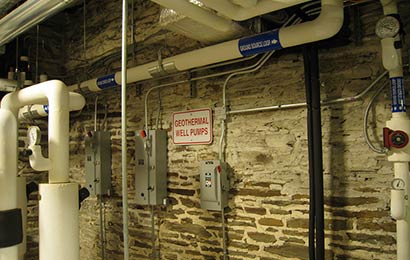 Ductwork and control boxes for a geothermal heating system in a stone-walled cellar.