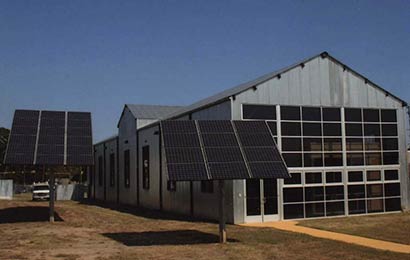Solar panels supported on poles next to an industrial building.