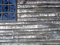 This is an image of unpainted oak clapboards, made by hand. The boards vary in width and thickness and have overlapping feather-edge ends. The silver-gray weathering adds to the random quality of the clapboards.