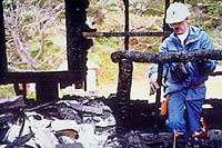 This is a detail image of architect, David Wark, evaluating the West log house after the devastating fire of late May, 1991.
