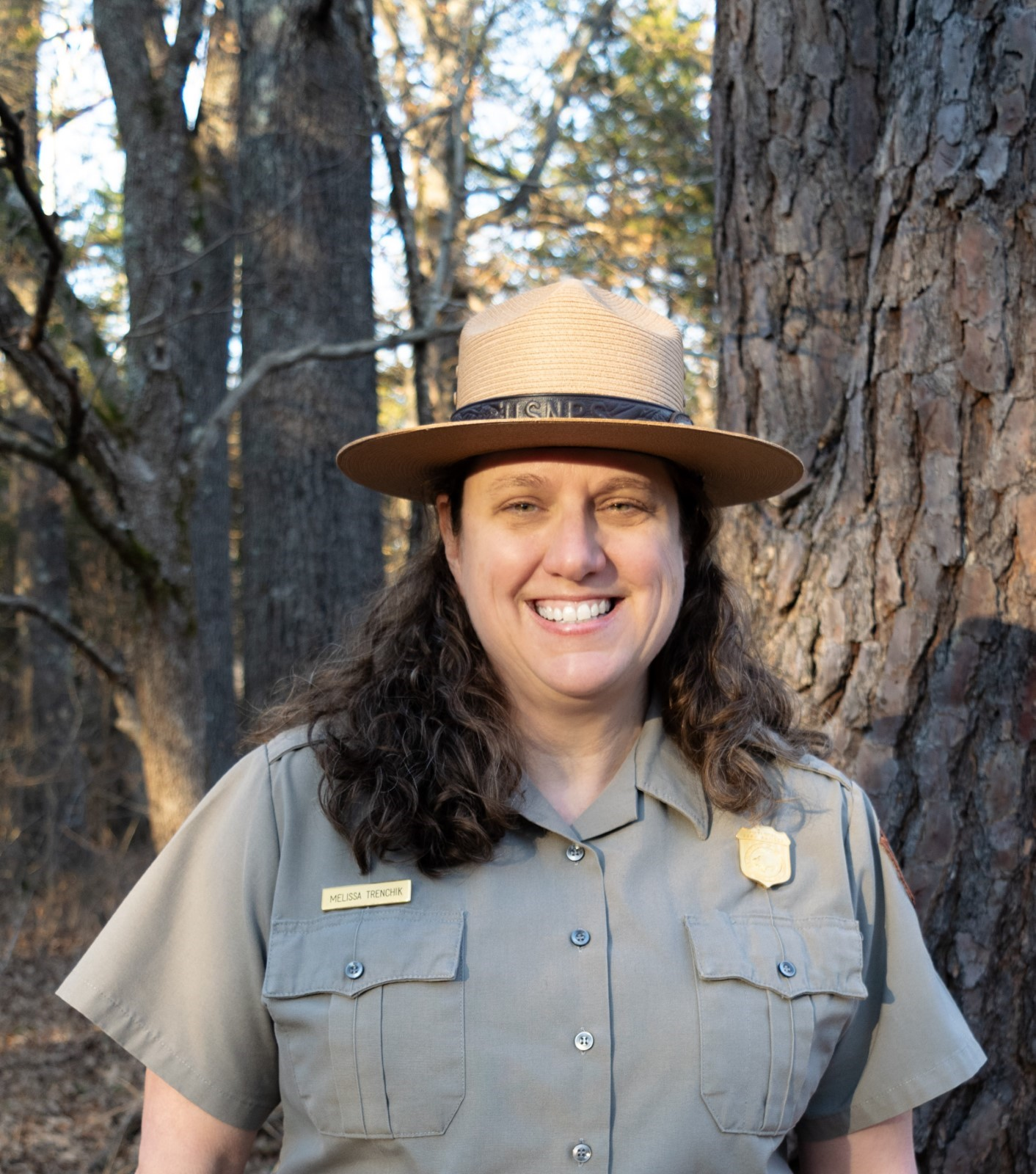 A smiling woman in a NPS uniform with trees in background