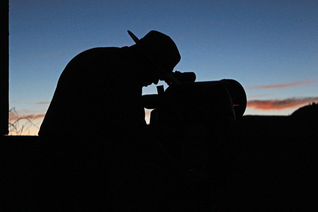 A silhouette of a person looking through a telescope