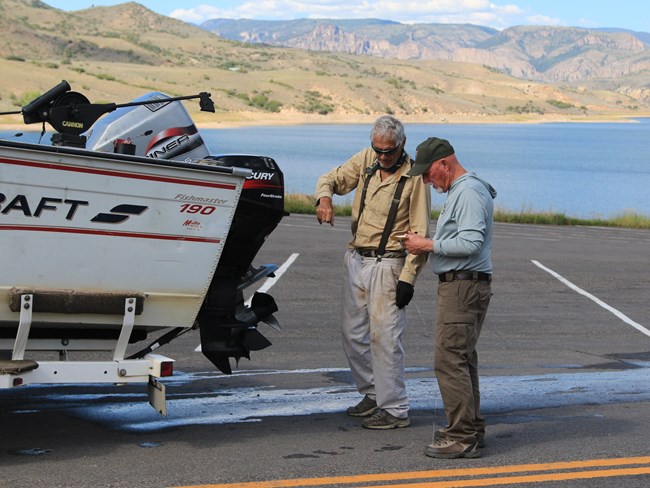 Two people stand beside a boat being inspected in a parking area.