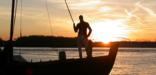 photo of a replica keelboat with a crew member on the bow at sunset