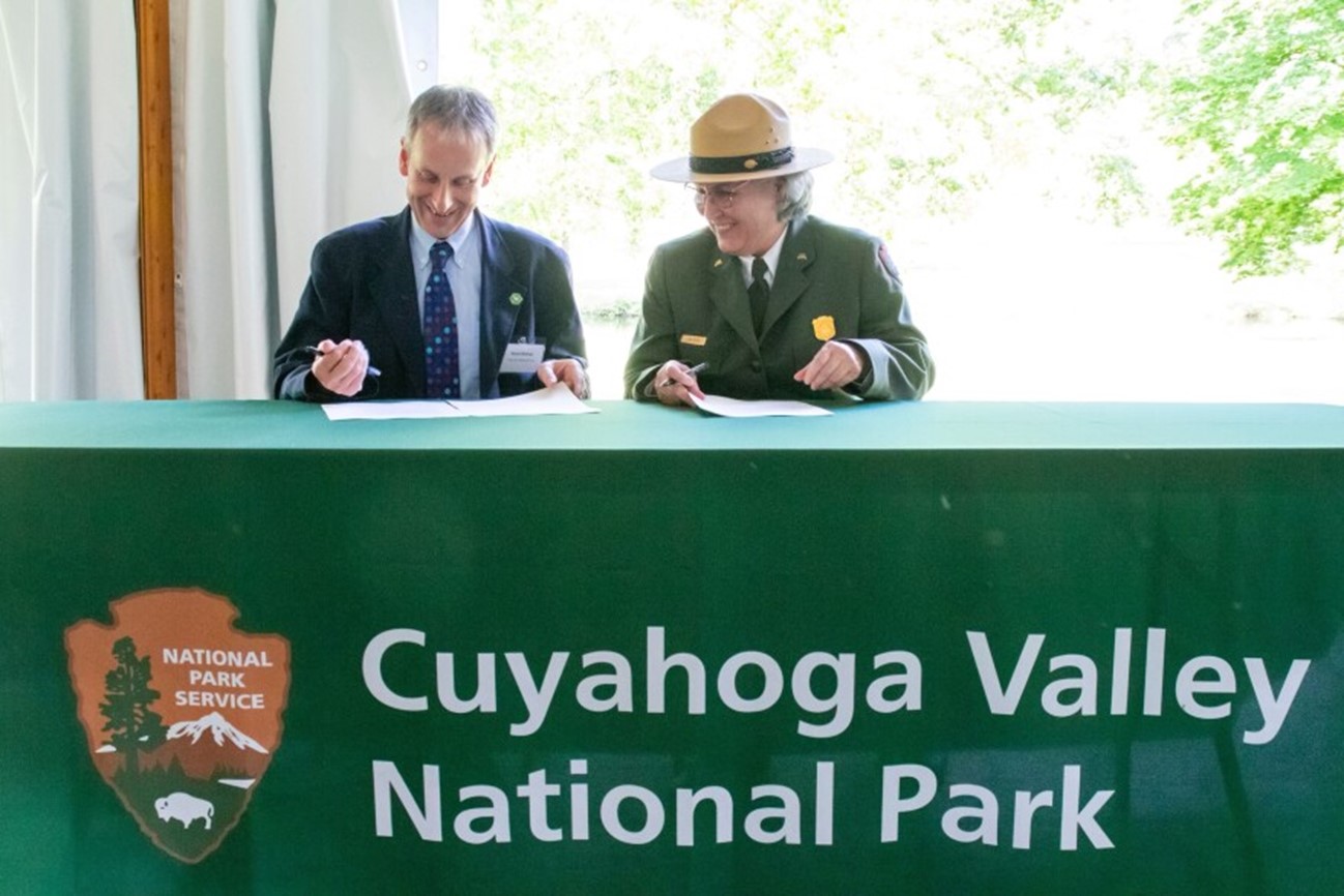 A man in a blue suit sits next to a woman in park ranger uniform at a table with green tablecloth and park logo