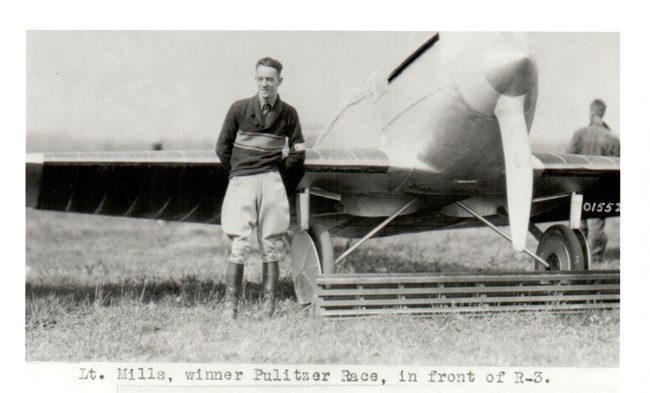 Black and white image of: Lieutenant H.H. Mills, winner of the Pulitzer Speed Trophy, posing in front of a Verville-Sperry racer.