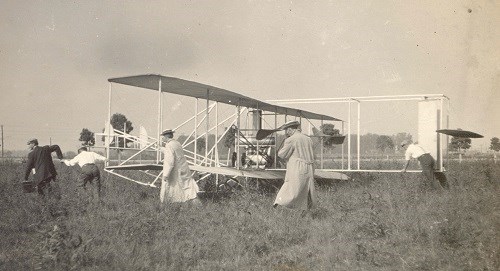 people holding onto an early airplane in a grassy field