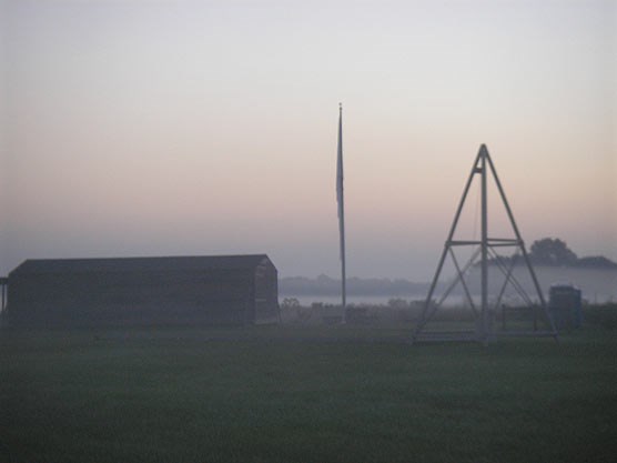 A large, one-story barn on the left, next to a triangular structure on the right with a flagpole in the middle.