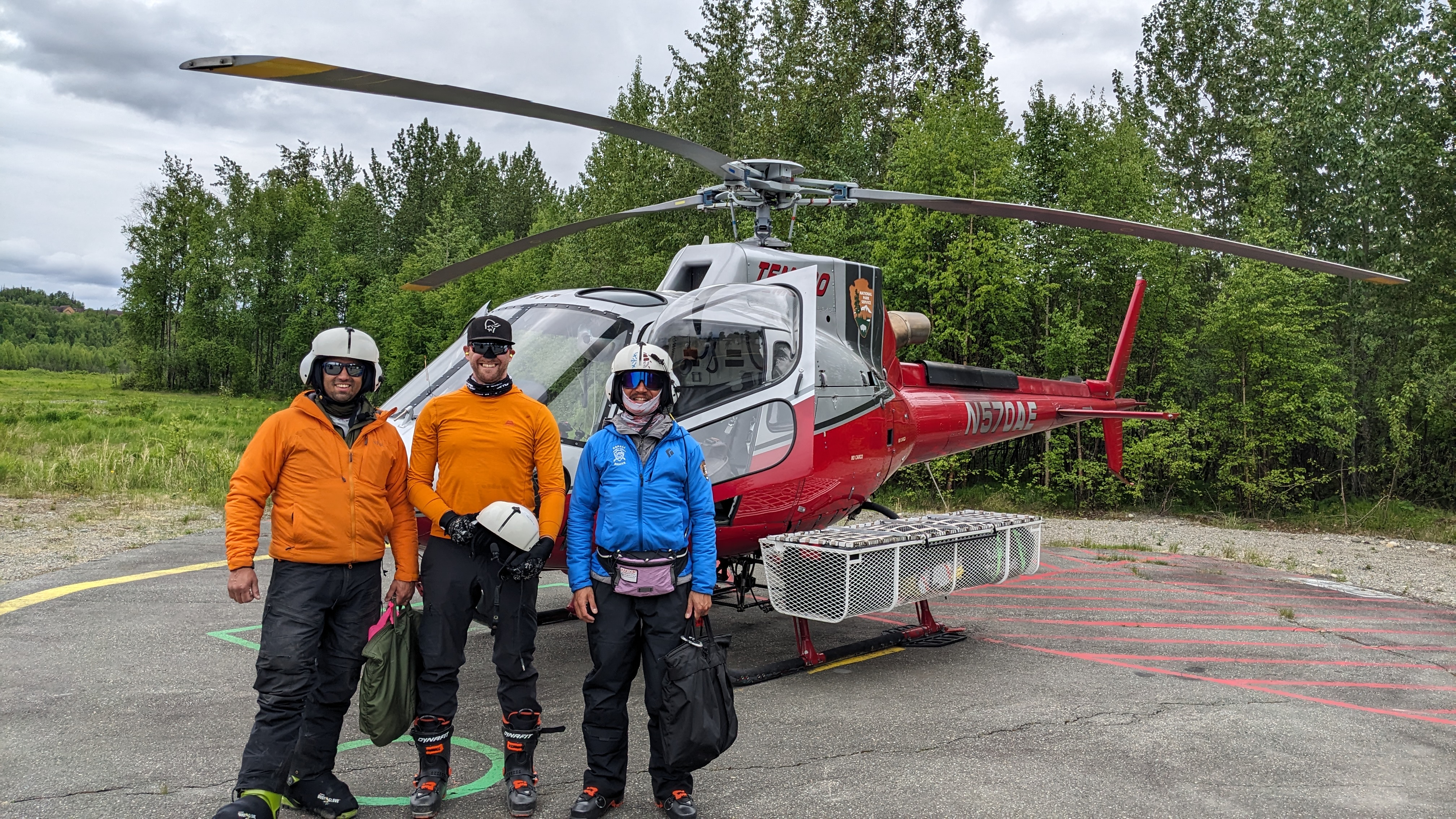 Three men with flight helments prepare to set into a red and grey helicopter