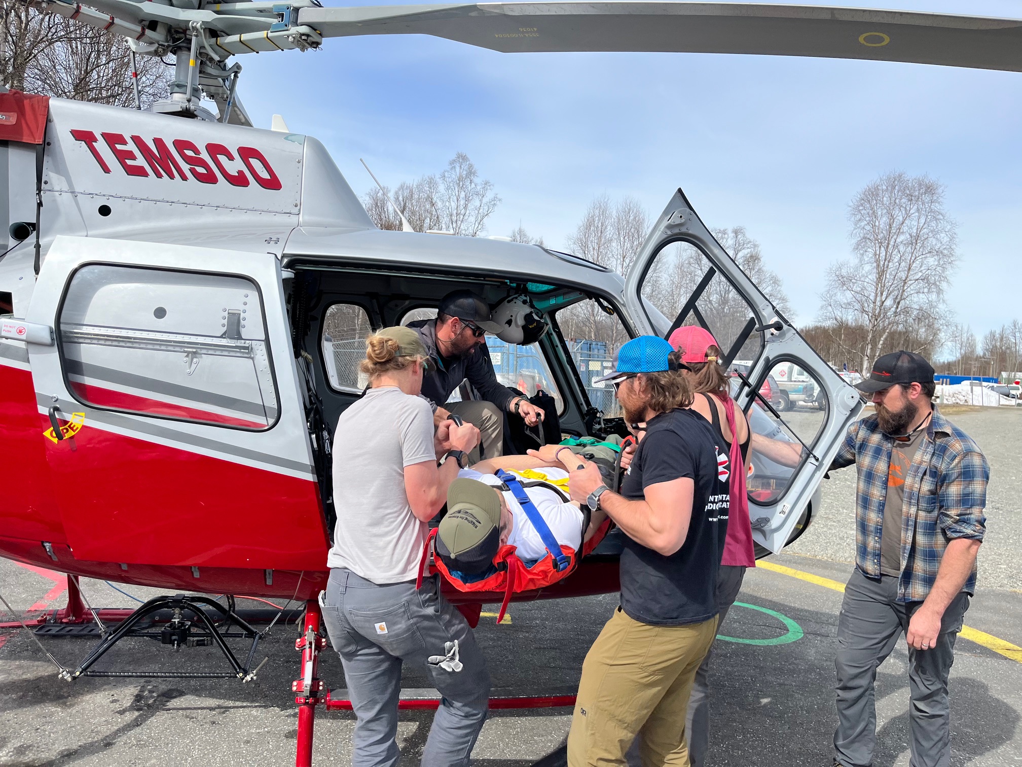 Multiple climbers load a patient strapped into a rescue litter into an open helicopter