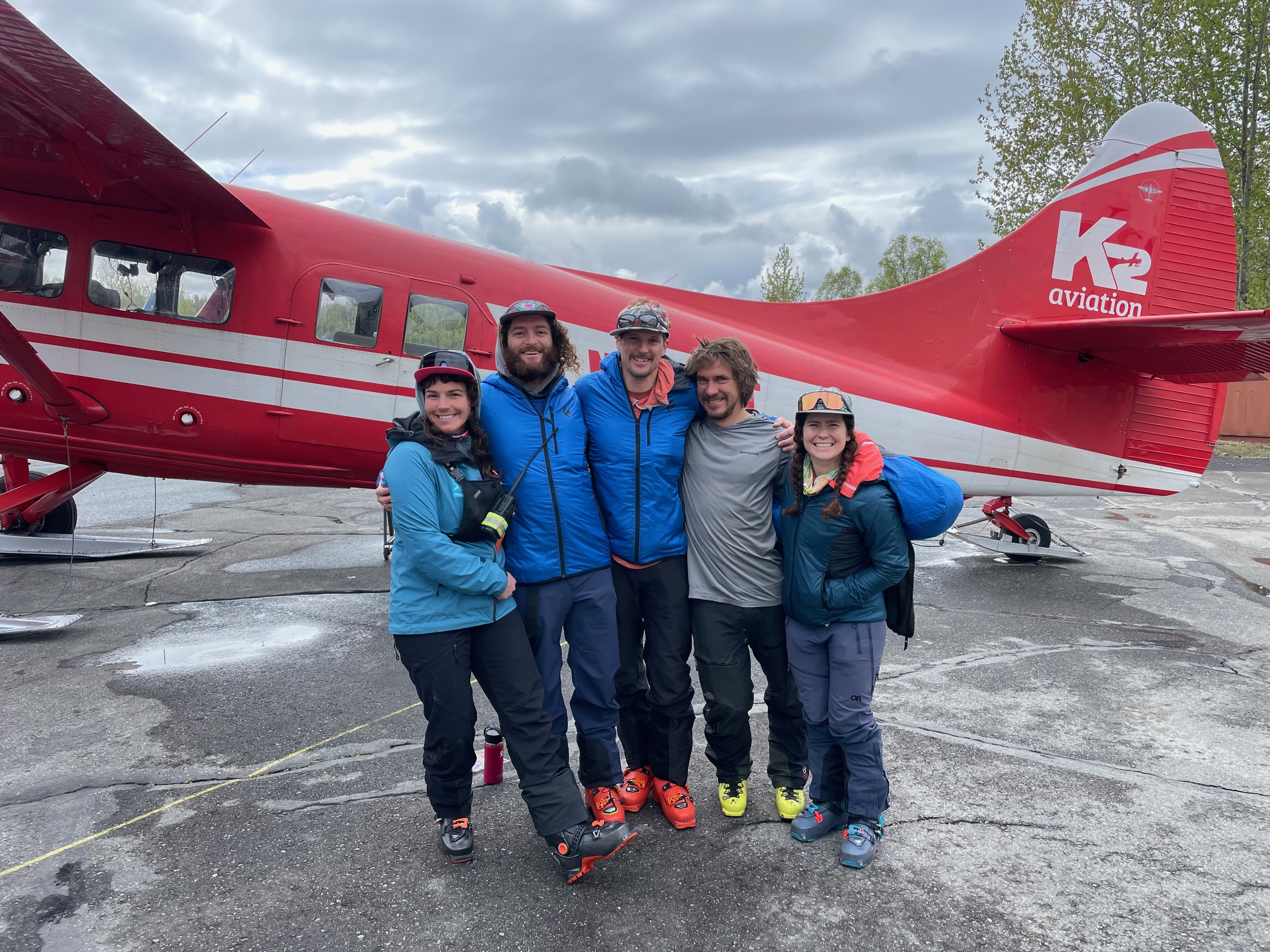 Five climbers huddle for a photo in front of a red and white airplane