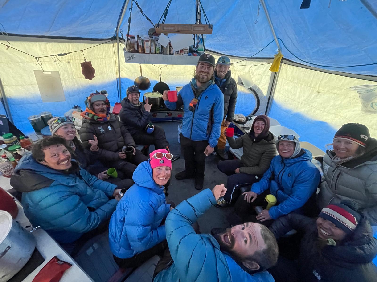 Twelve climbers in puffy coats huddle in a tent