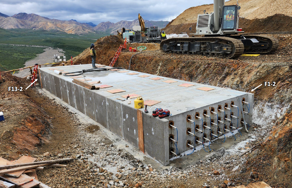 A construction worker stands on a large, rectangular grey cement structure set into a rocky surface.