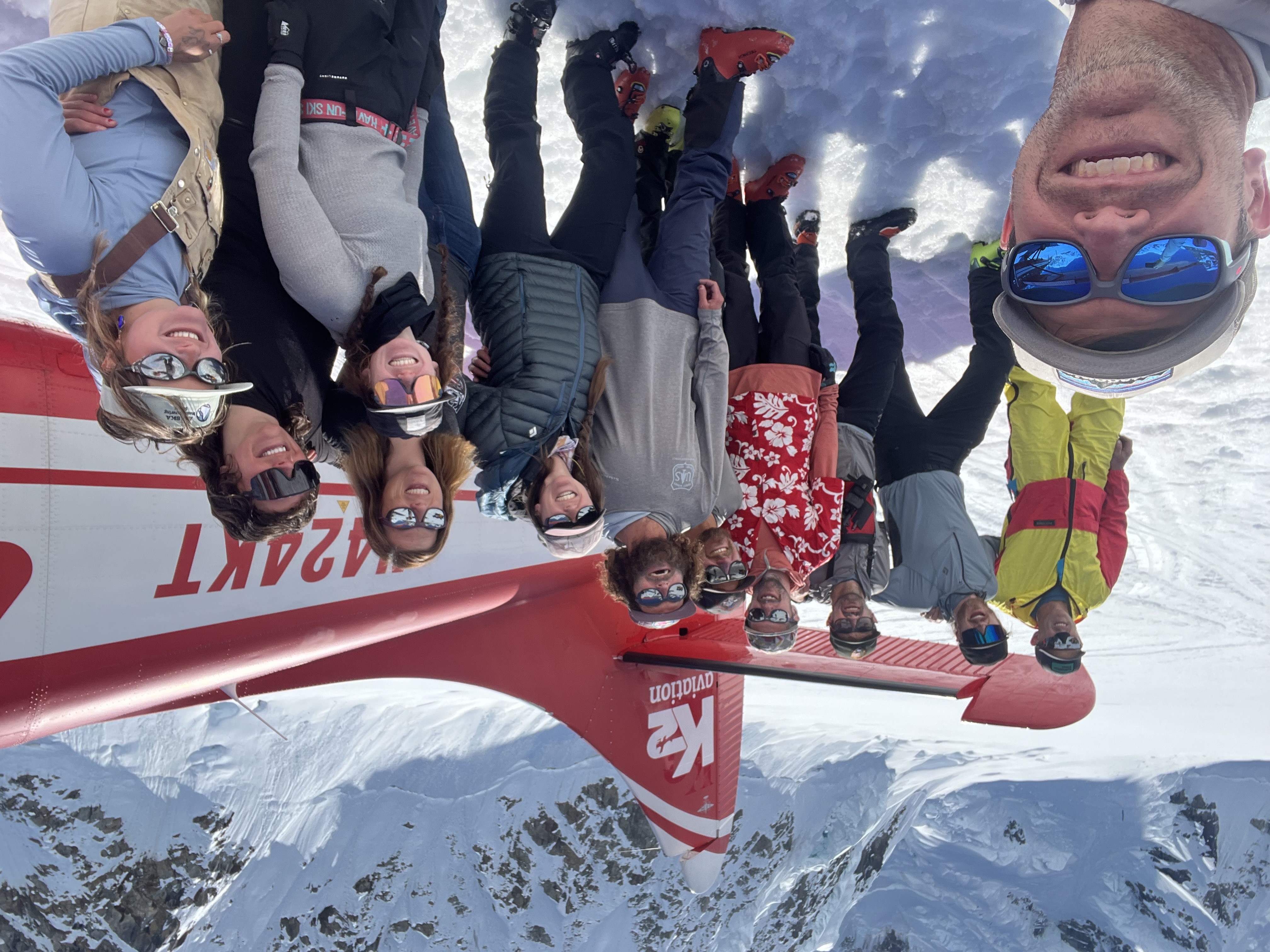 Twelve climbers pose for a photo near the tail of a red and white airplane