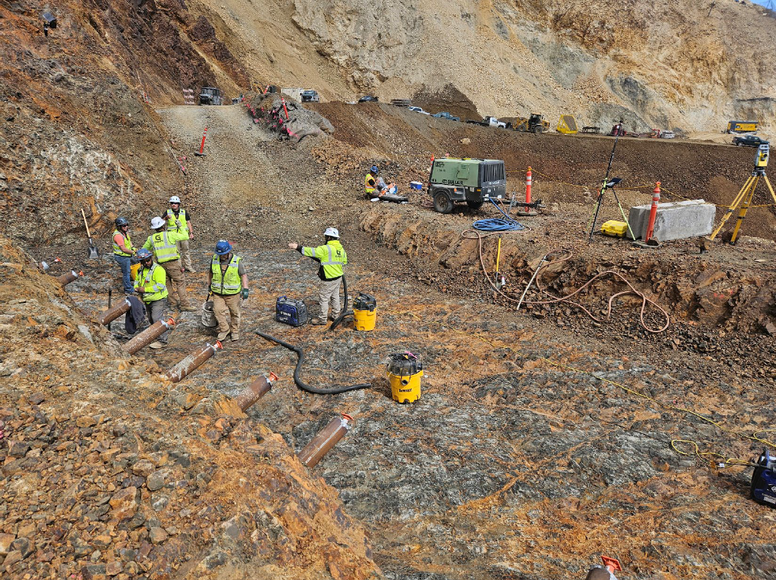 Seven people in hi-vis vests work on rocky terrain