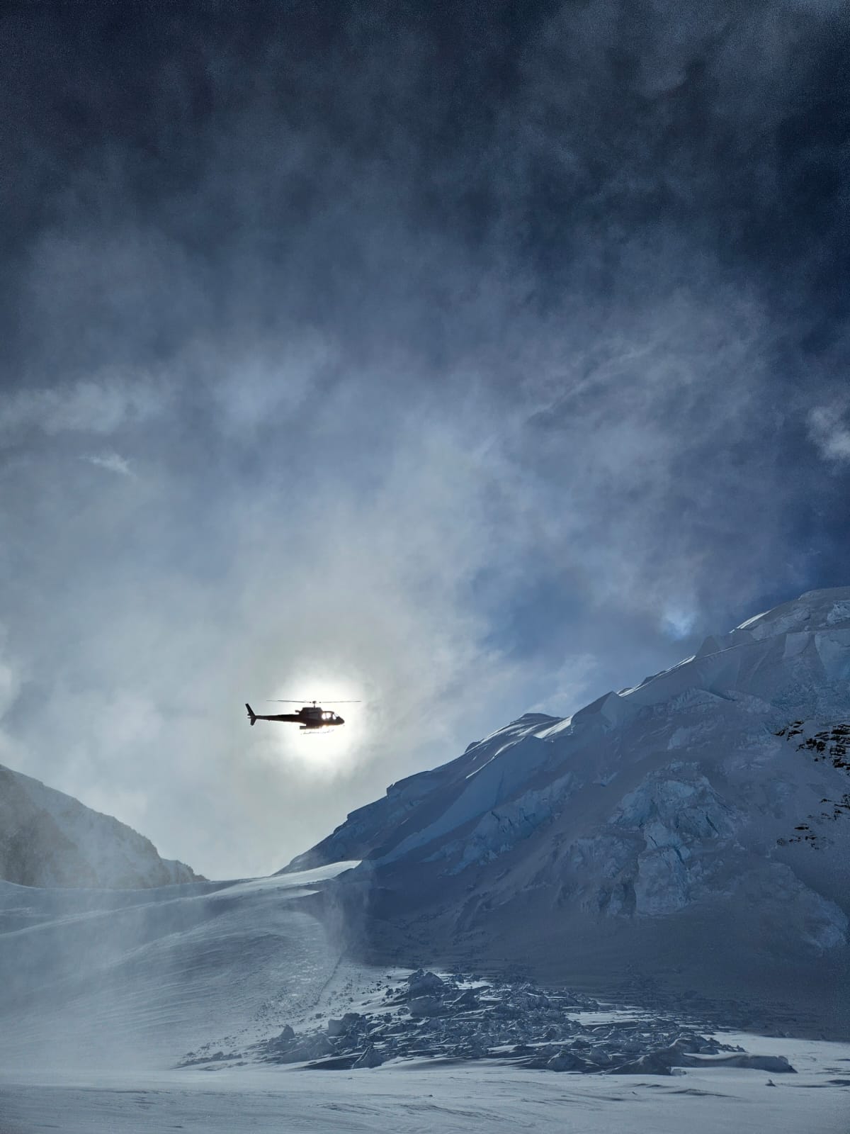 The silhouette of a helicopter in the sky above a glacial ridge