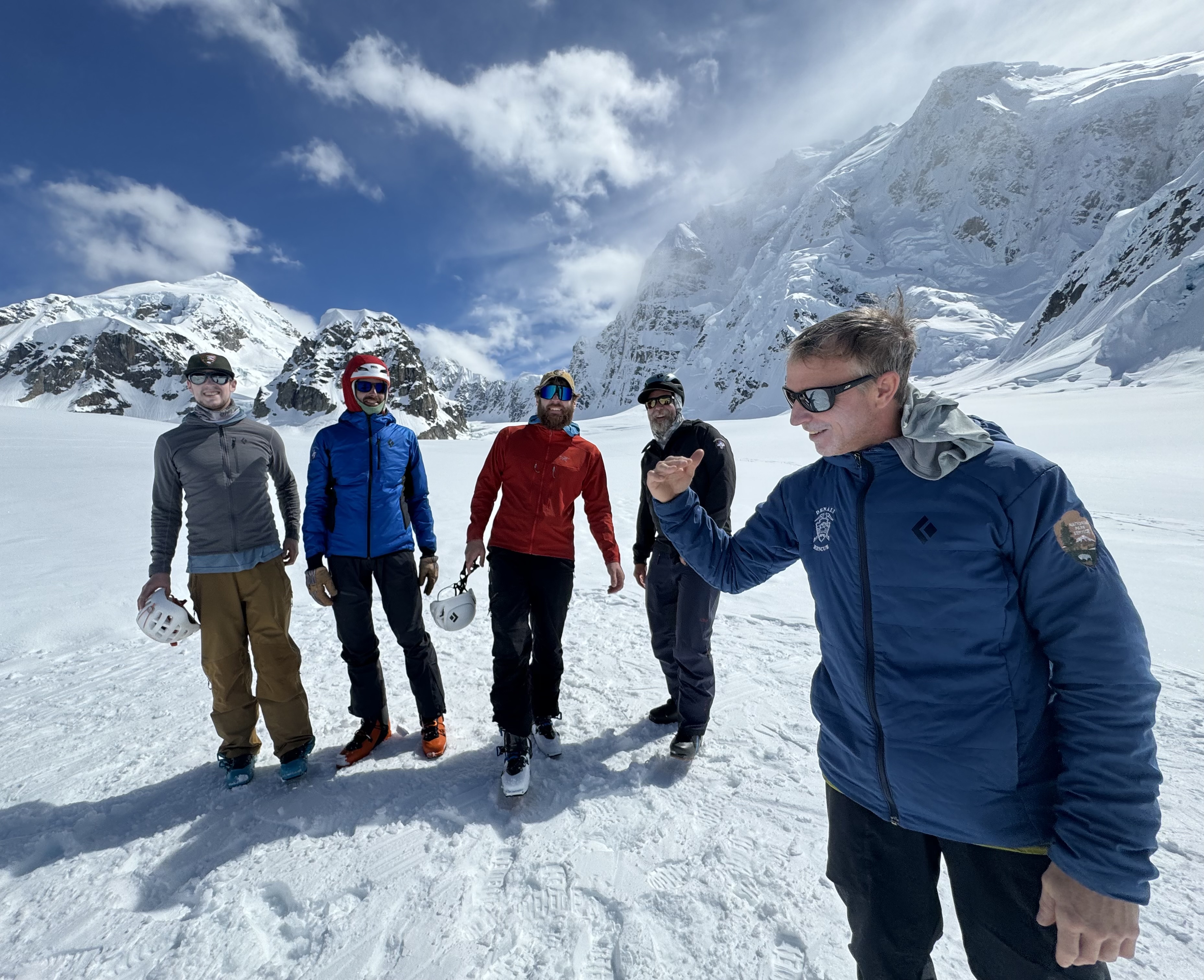 Five men stand on a glacier surrounded by peaks