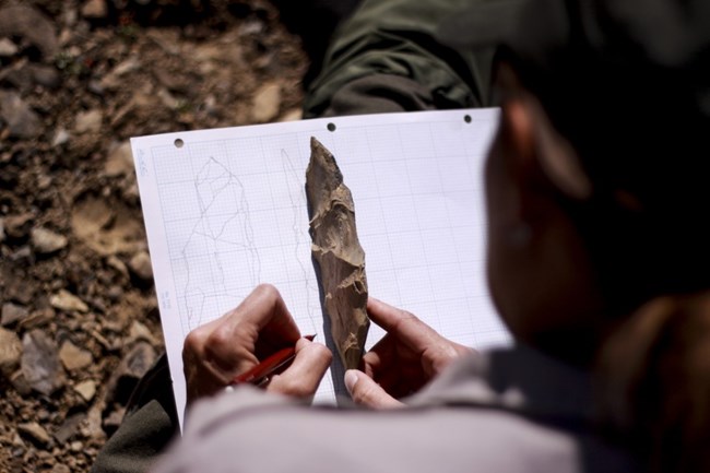 An archeologist sketches an artifact on graph paper.