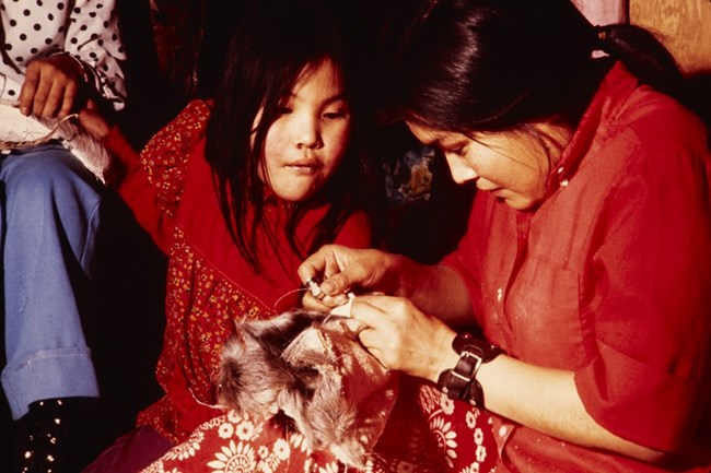 An Alaska Native woman in Ambler, near Kobuk Valley National Park, teaches a young girl how to sew caribou skin mukluks.