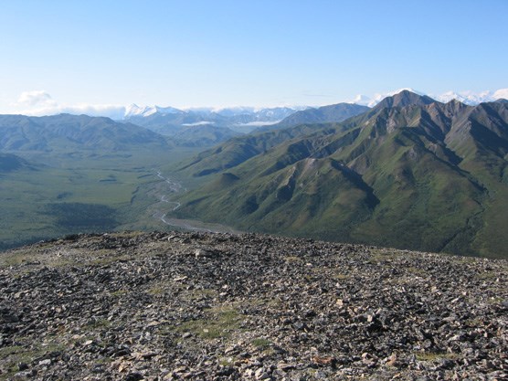 a wide valley with a shallow creek running down the middle, surrounded by rugged mountains on either side