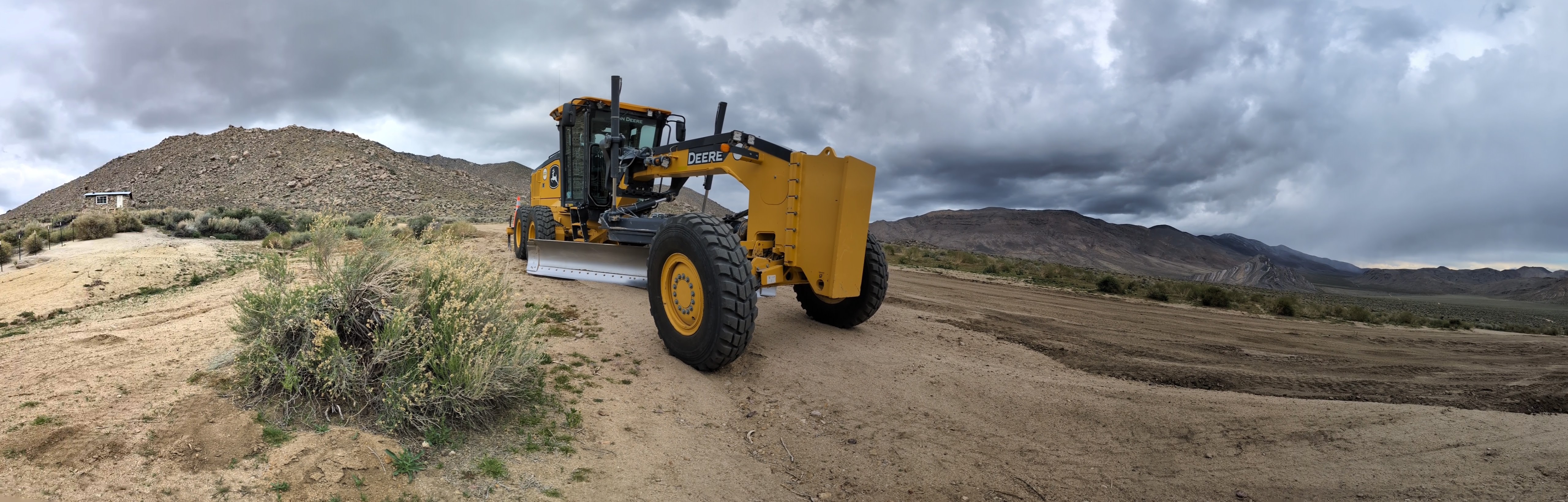 Panoramic photo of a large yellow machine in a bare desert landscape with dramatic clouds.