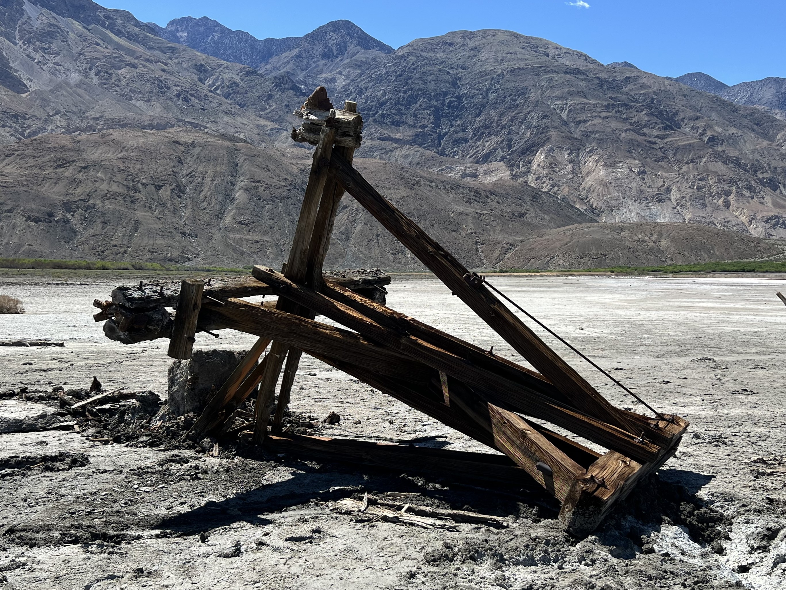 A wooden structure is toppled over on flat white ground. Dark mountains are in the background.