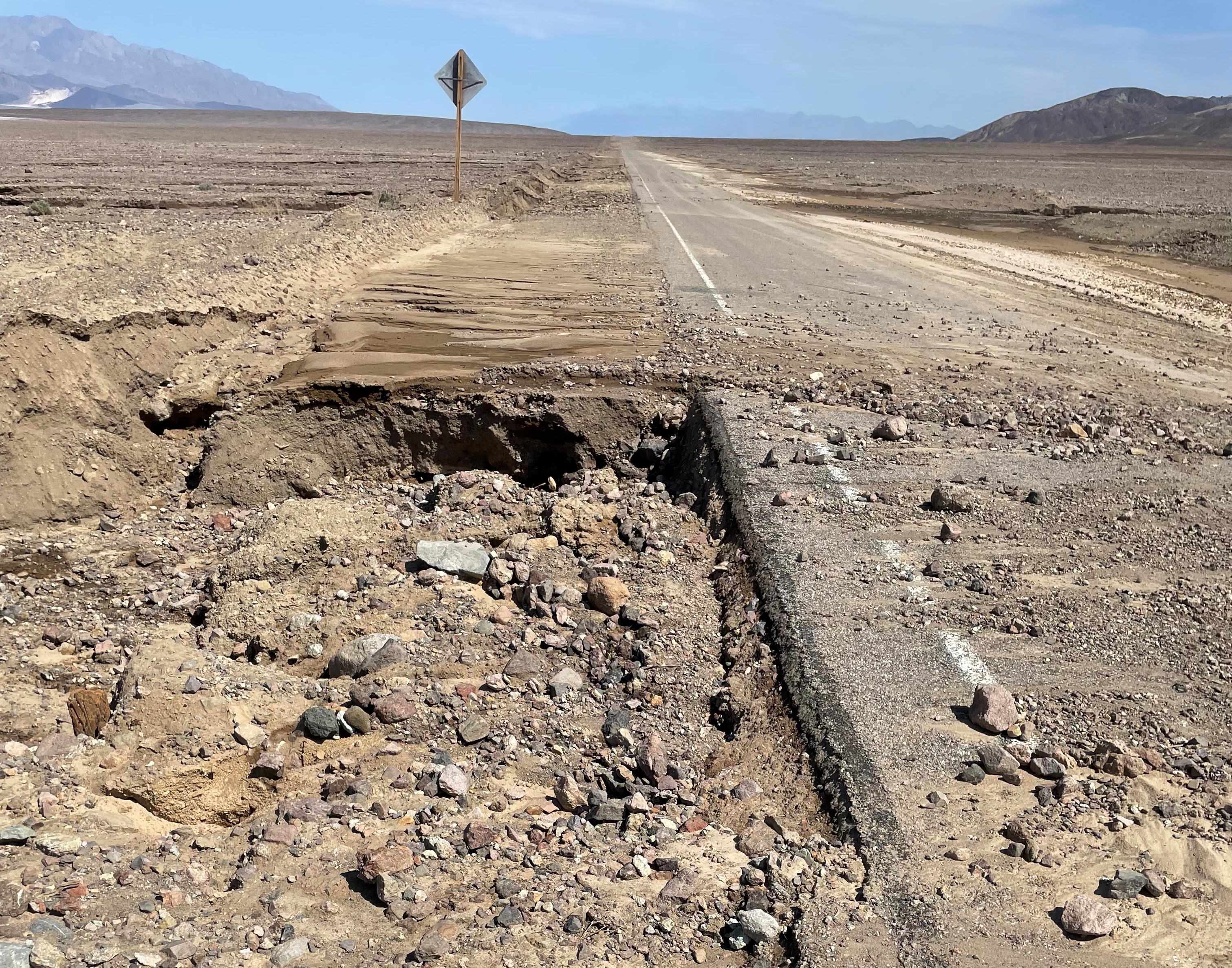 There are dirt and rocks on a paved road, with an eroded shoulder.