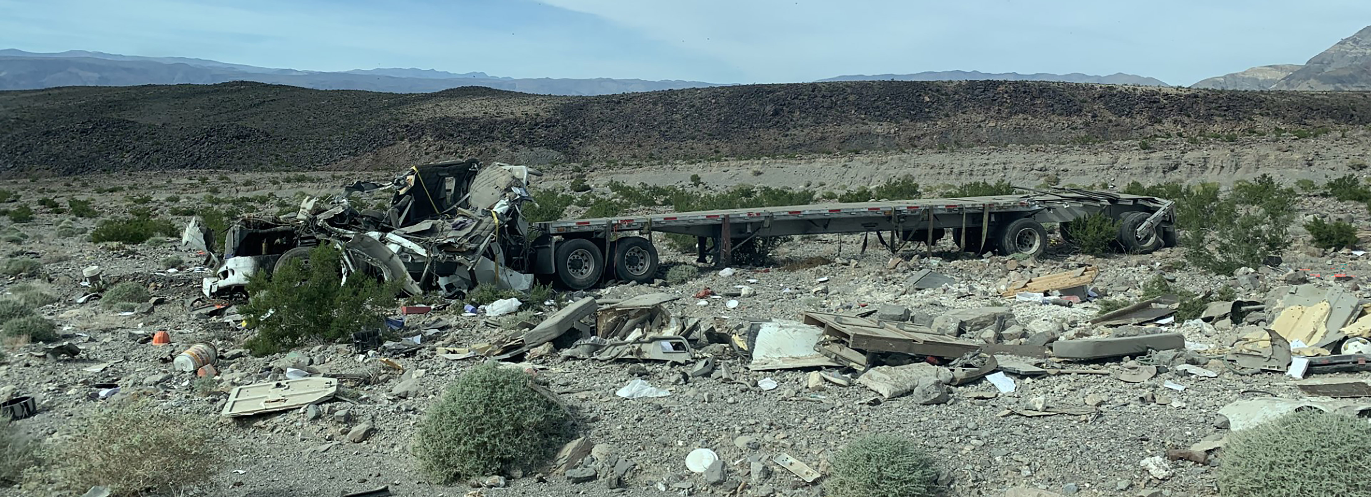 Crashed semi truck in rocky area of a valley. Truck is collapsed and debris is scattered around the ground.