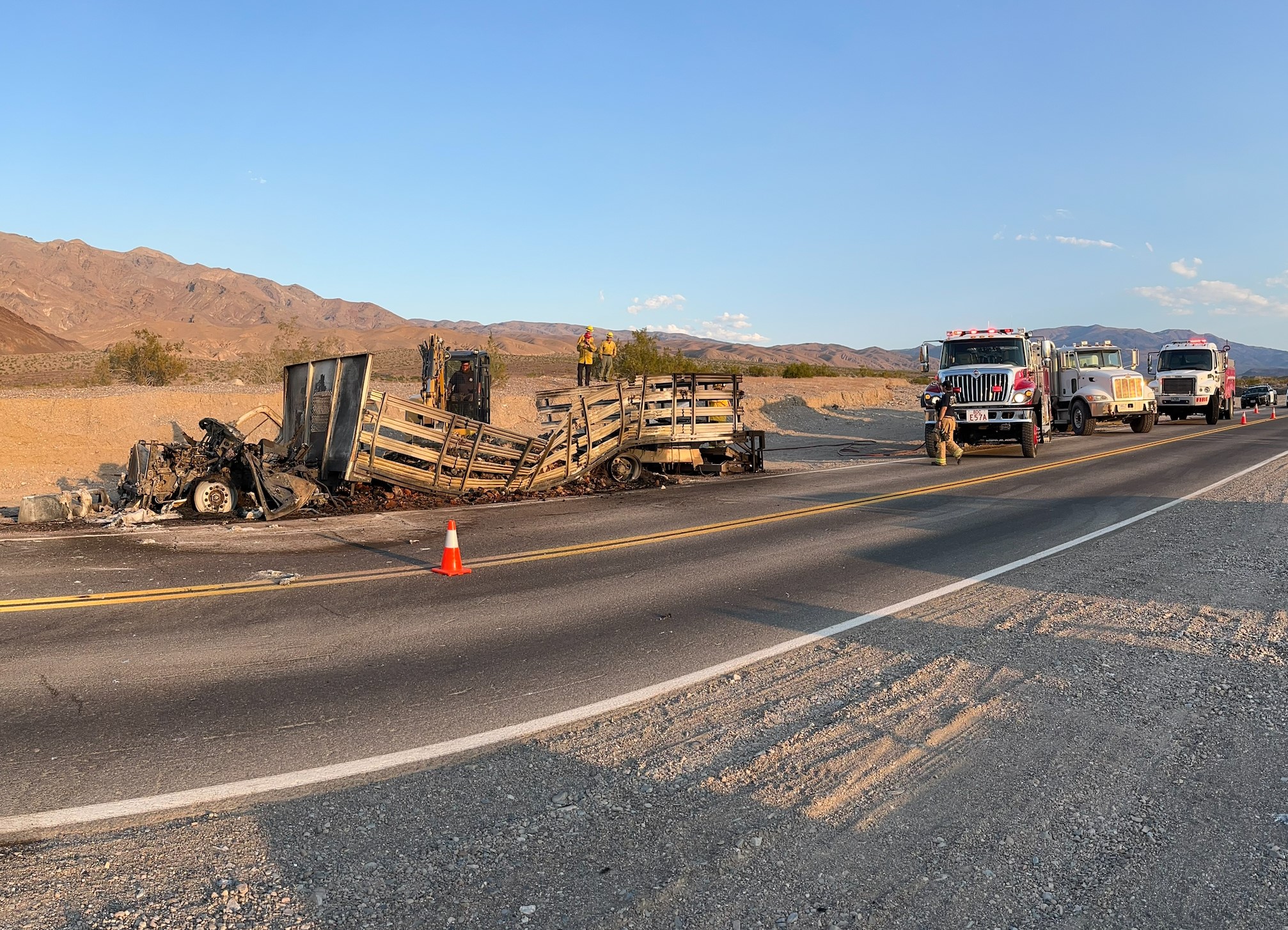 A little black smoke rises from a burnt truck with a stake-bed. Several fire engines are parked to the right.