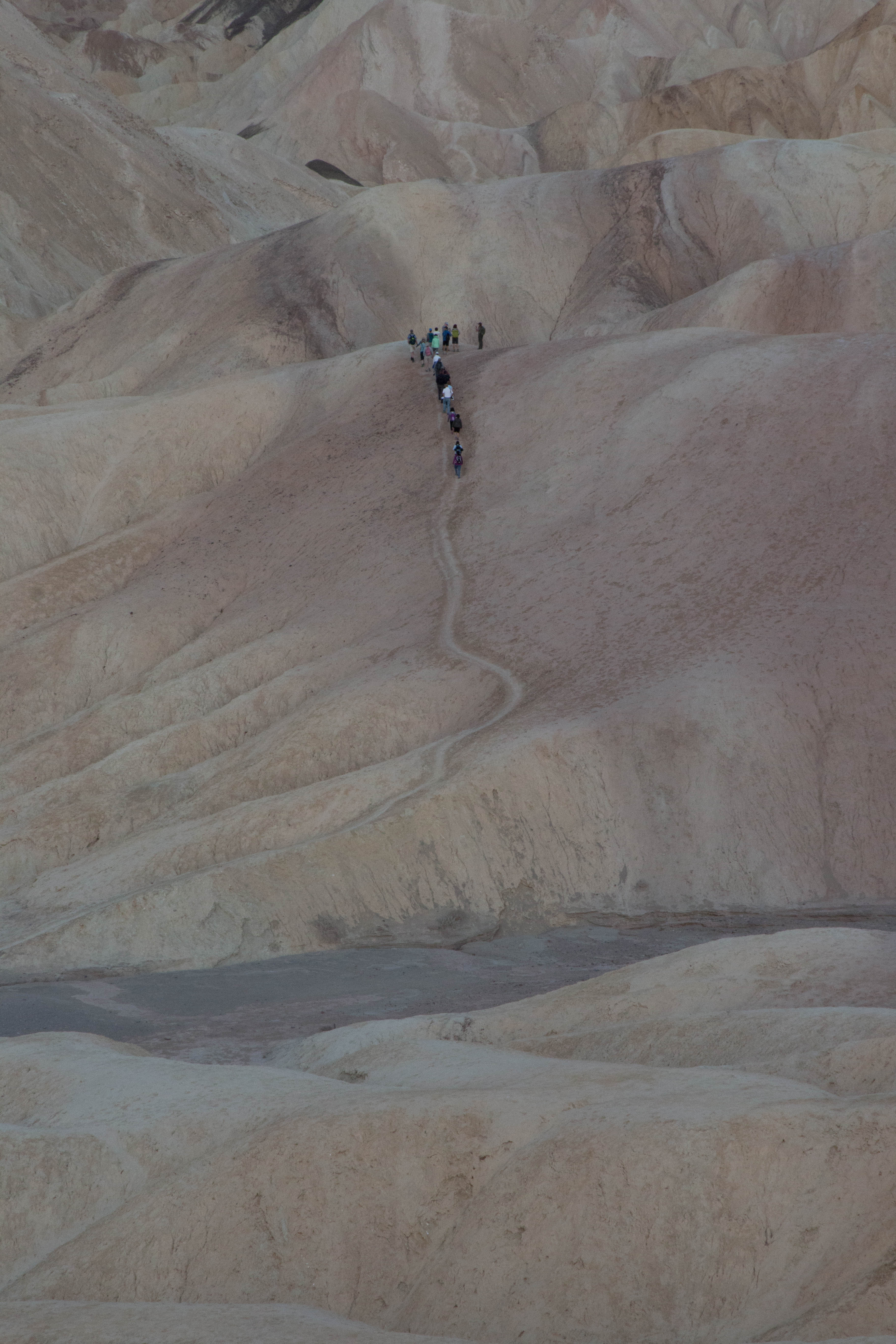 A group of hikers travel up a path through highly eroded desert hills.