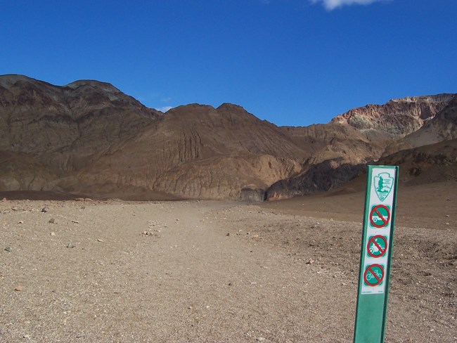 A green wilderness barrier with symbols prohibiting motor vehicles and bicycles at the start of a canyon hike.