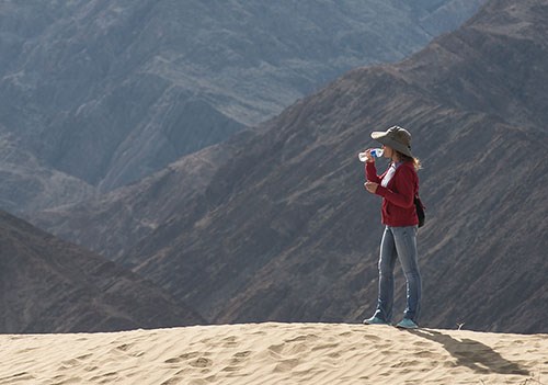 Aa woman drinks water while hiking on the dunes.