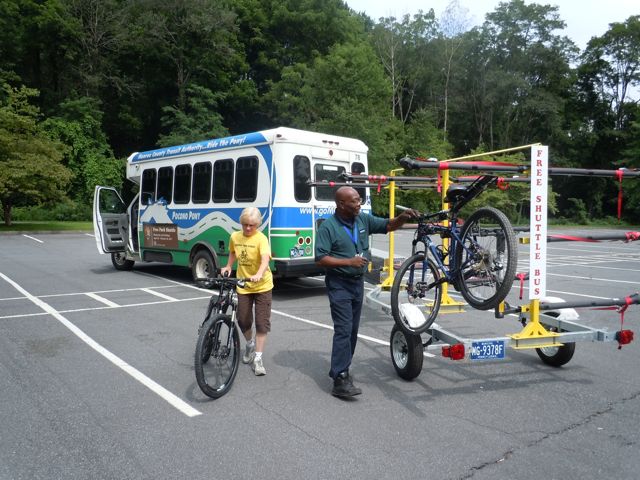 A shuttle towing a trailer and people putting bikes on the trailer.