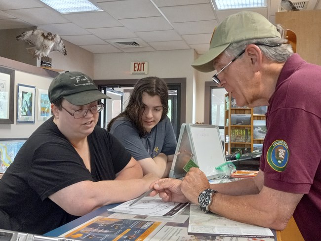 A volunteer helping two visitors at an information desk.